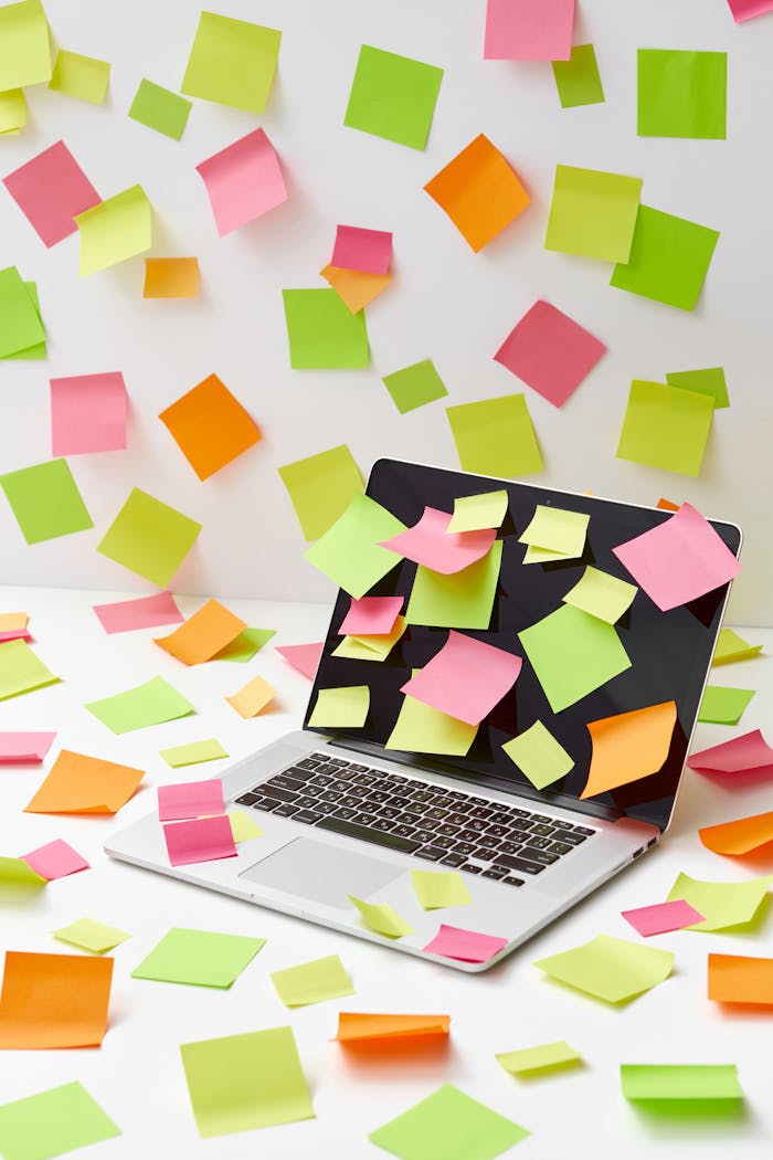 Laptop covered in sticky notes, with vibrant papers scattered around, captures creative chaos.